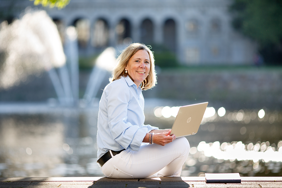 Blonde Frau mit Laptop vor Brunnen