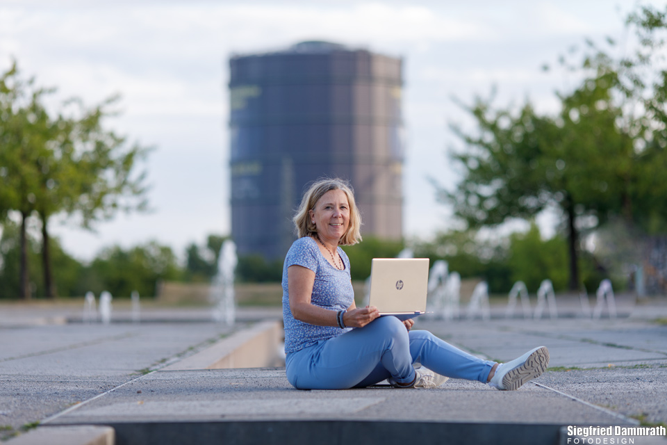 Blonde Frau mit Laptop vor einem Gasometer