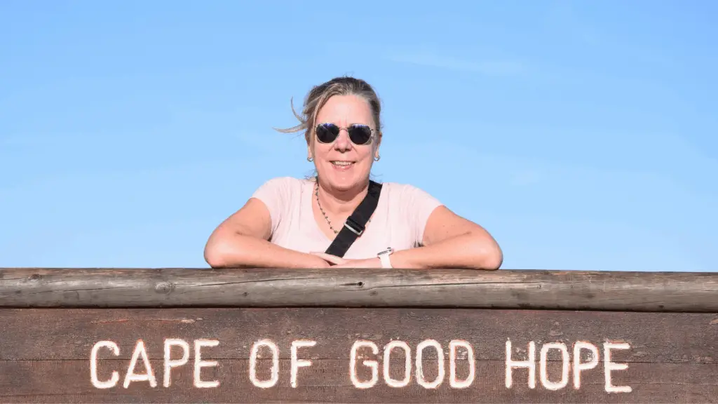 Blonde Frau mit Sonnenbrille steht am Schild am Kap der guten Hoffnung.